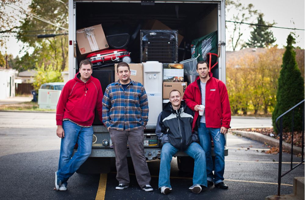 Four Devbridge employees in front of a packed moving truck